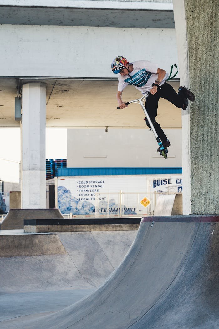 Young man performing a scooter trick on a ramp in an urban skate park.