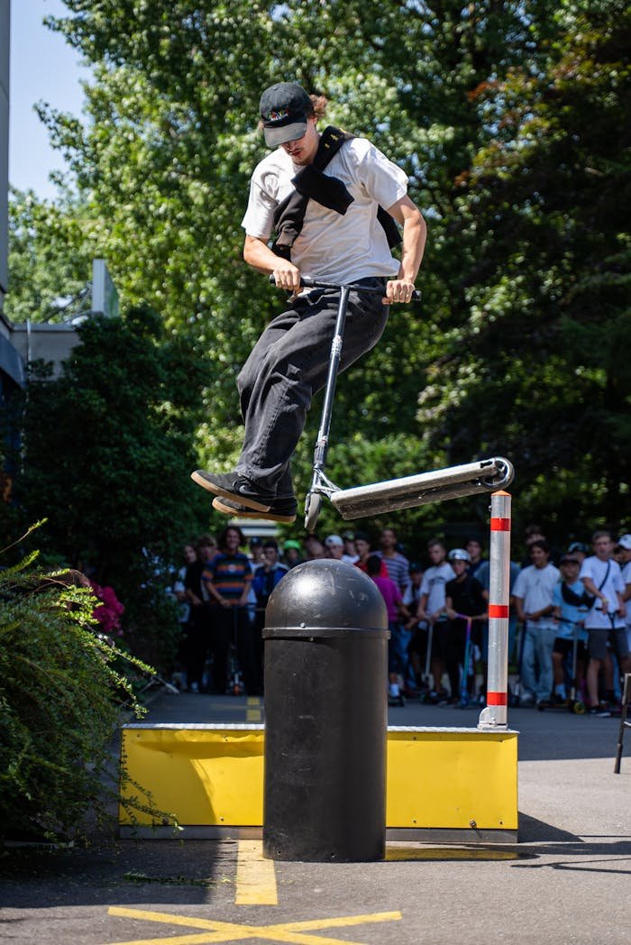 Man performing a high-energy trick on a kick scooter in an urban park setting.